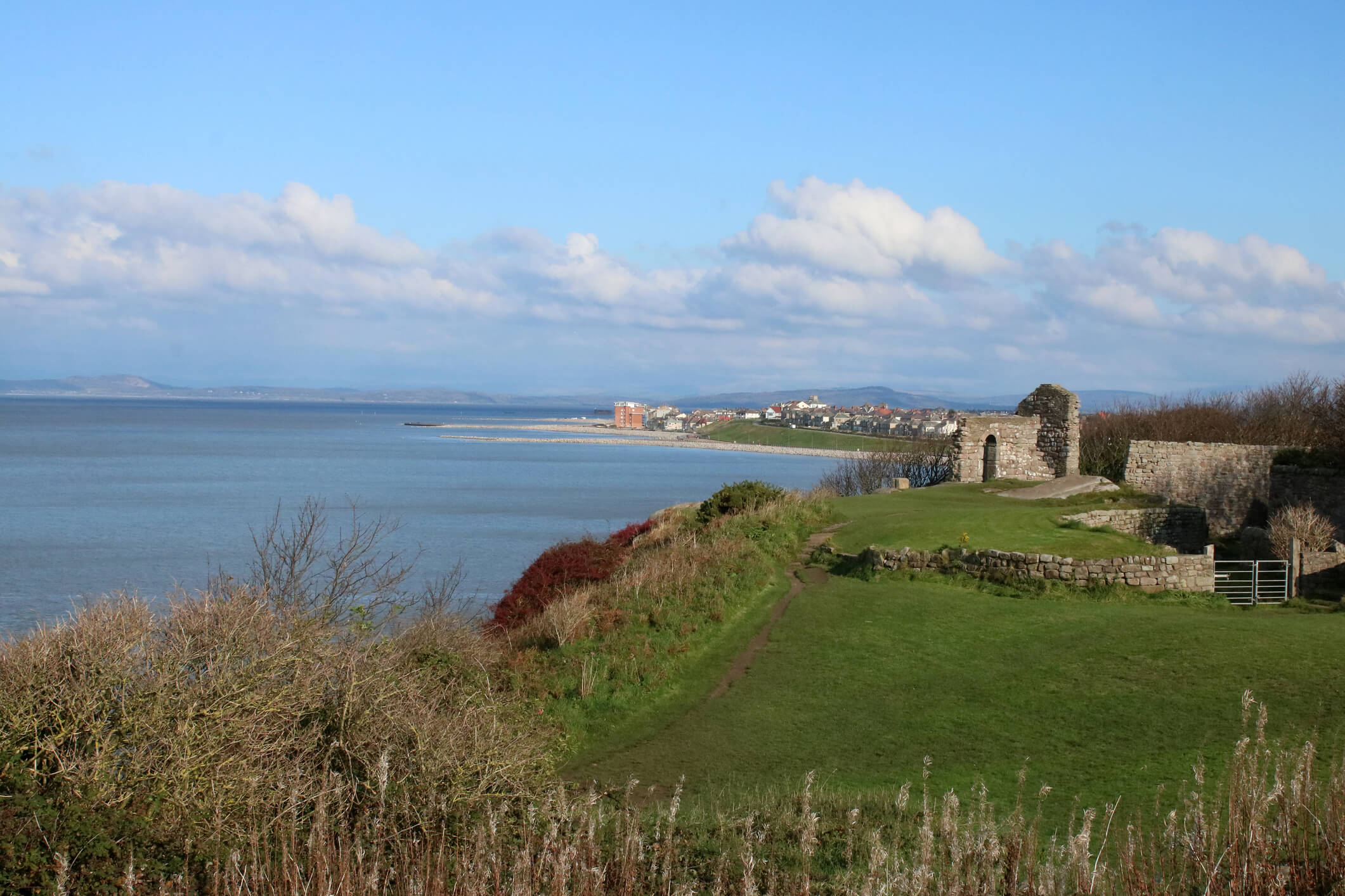 View from cliff top path leading to St Patrick`s Chapel, ruins of ancient building, Heysham with view to Morecambe along edge of Morecambe Bay and hills beyond